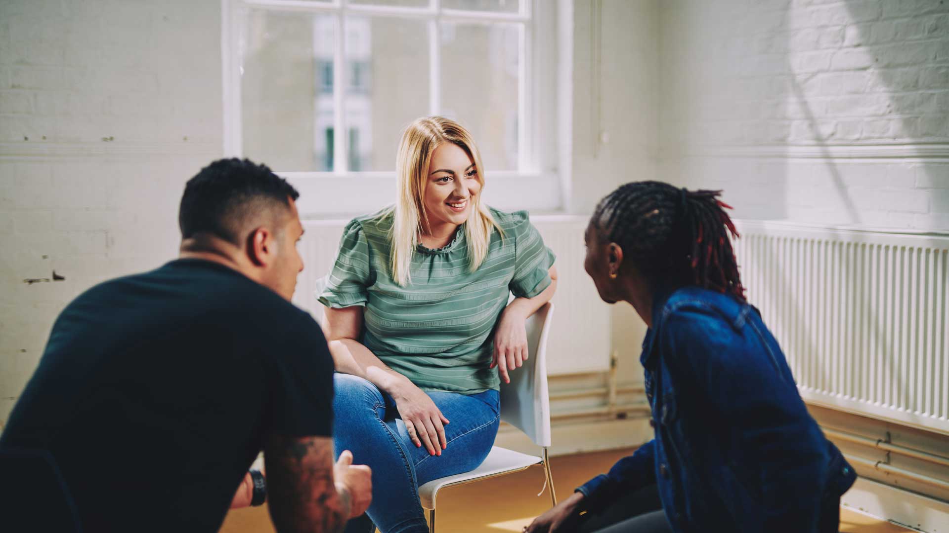 woman smiling sitting on a chair talking to two people