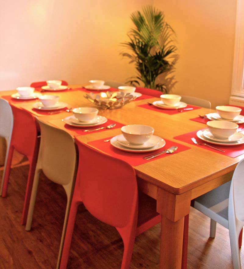 A dining table with orange and beige chairs. The table is laid with white plates and bowls