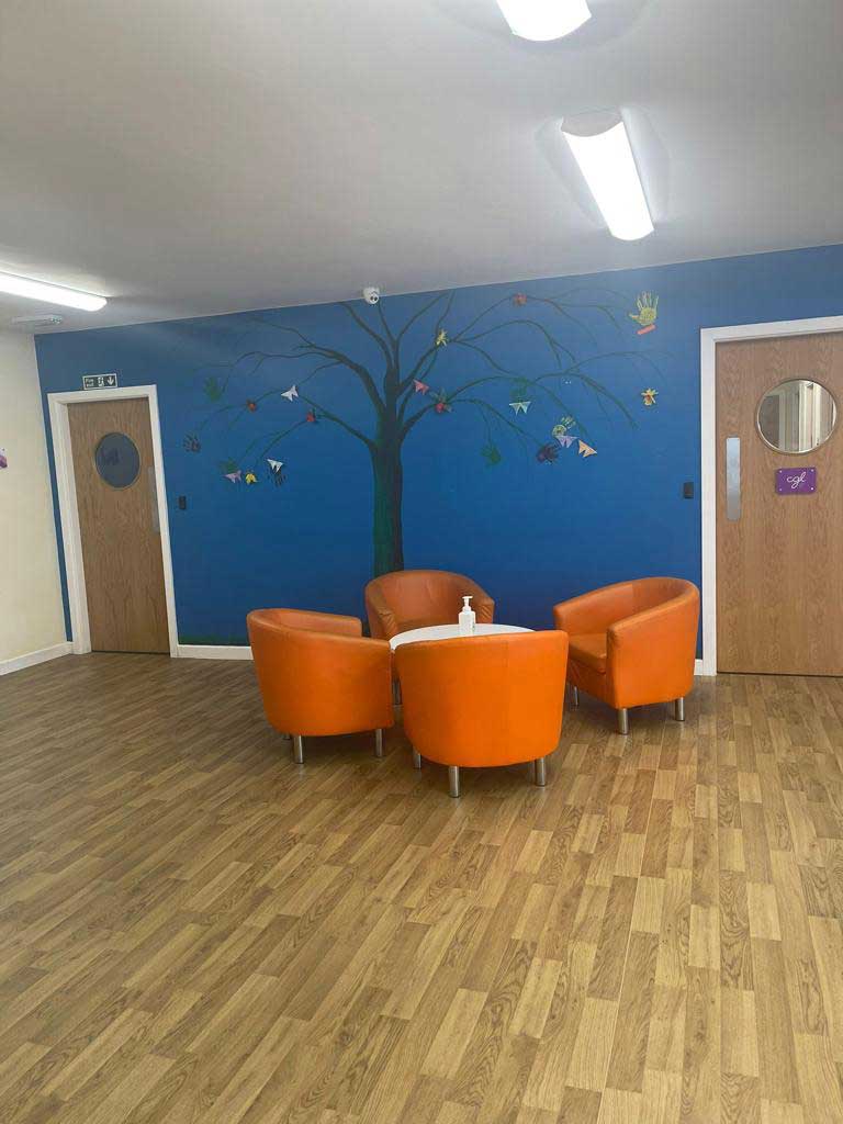 Reception area - a room with four orange tub chairs, a blue wall and doors either side of the chairs