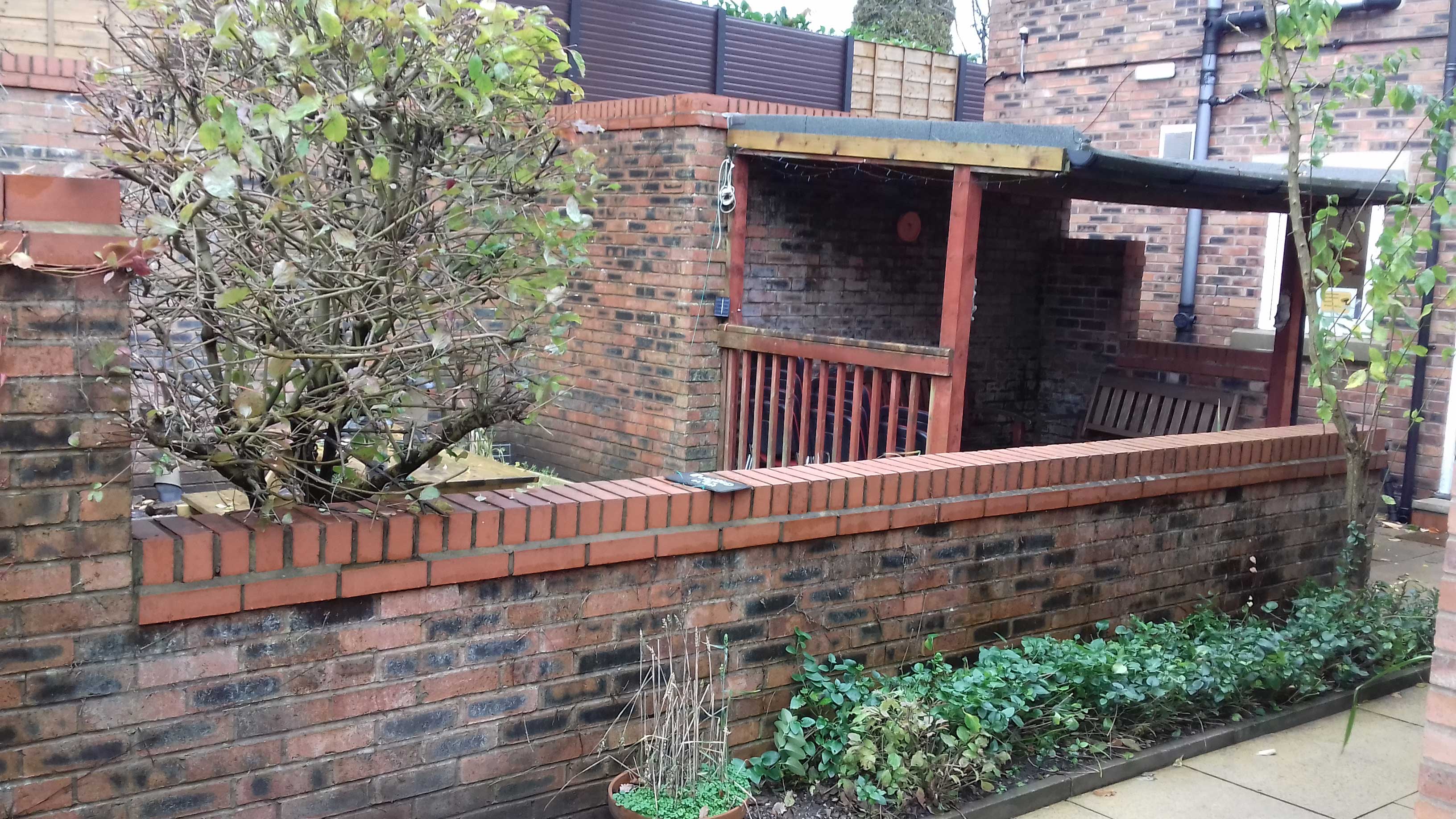 Leigh bank - garden. A patio area with a shelter, a brick wall a tree and some plants