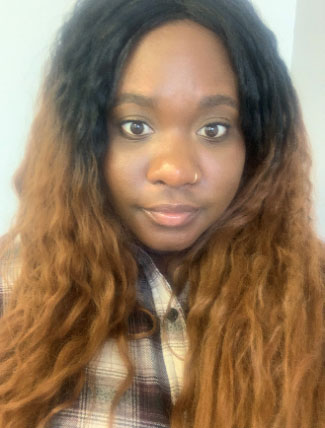 A woman smiling at the camera wearing a plaid shirt and her hair down