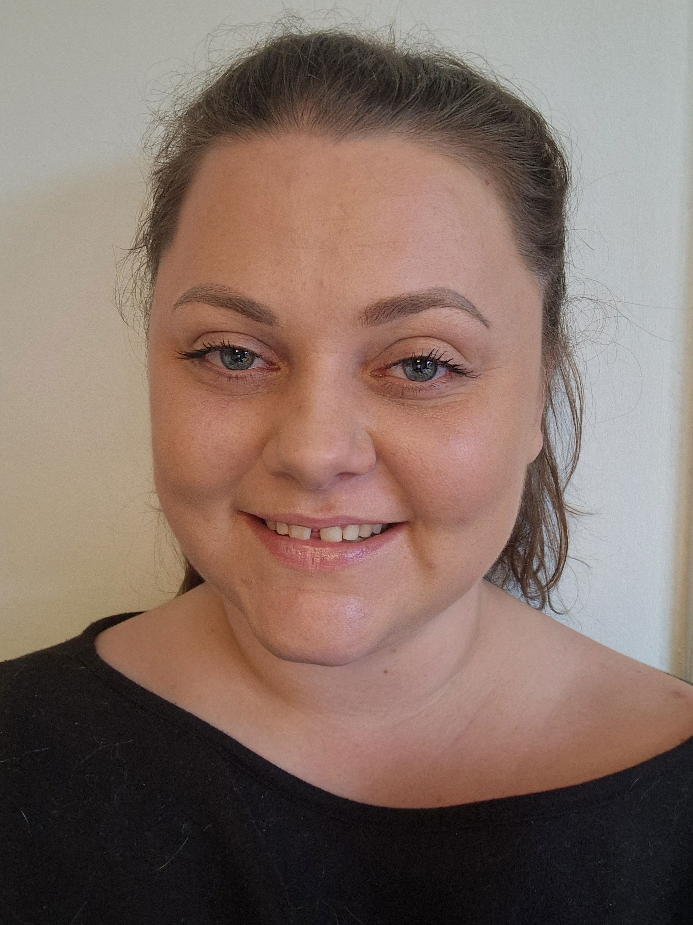 A woman wearing a black t-shirt, smiling at the camera with her hair pulled back into a ponytail