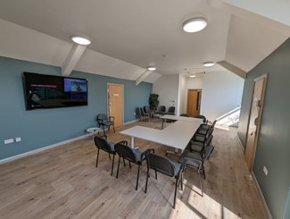 A table with chairs around the outside. There is a TV on the wall.