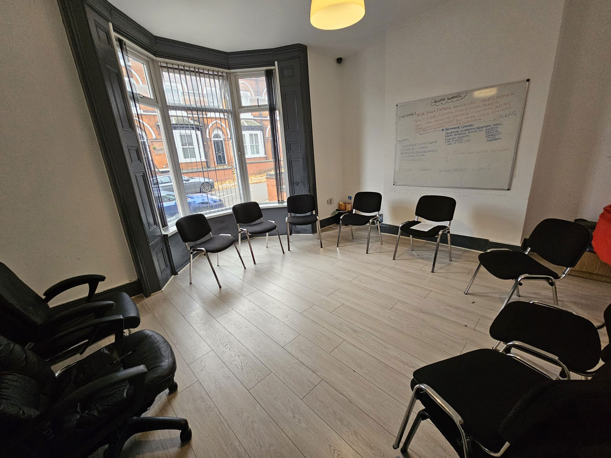 A room with big bay windows on one wall. There are chairs lining the edge of the room.