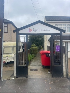 A black archway is over a path. The St Luke's logo is on the top