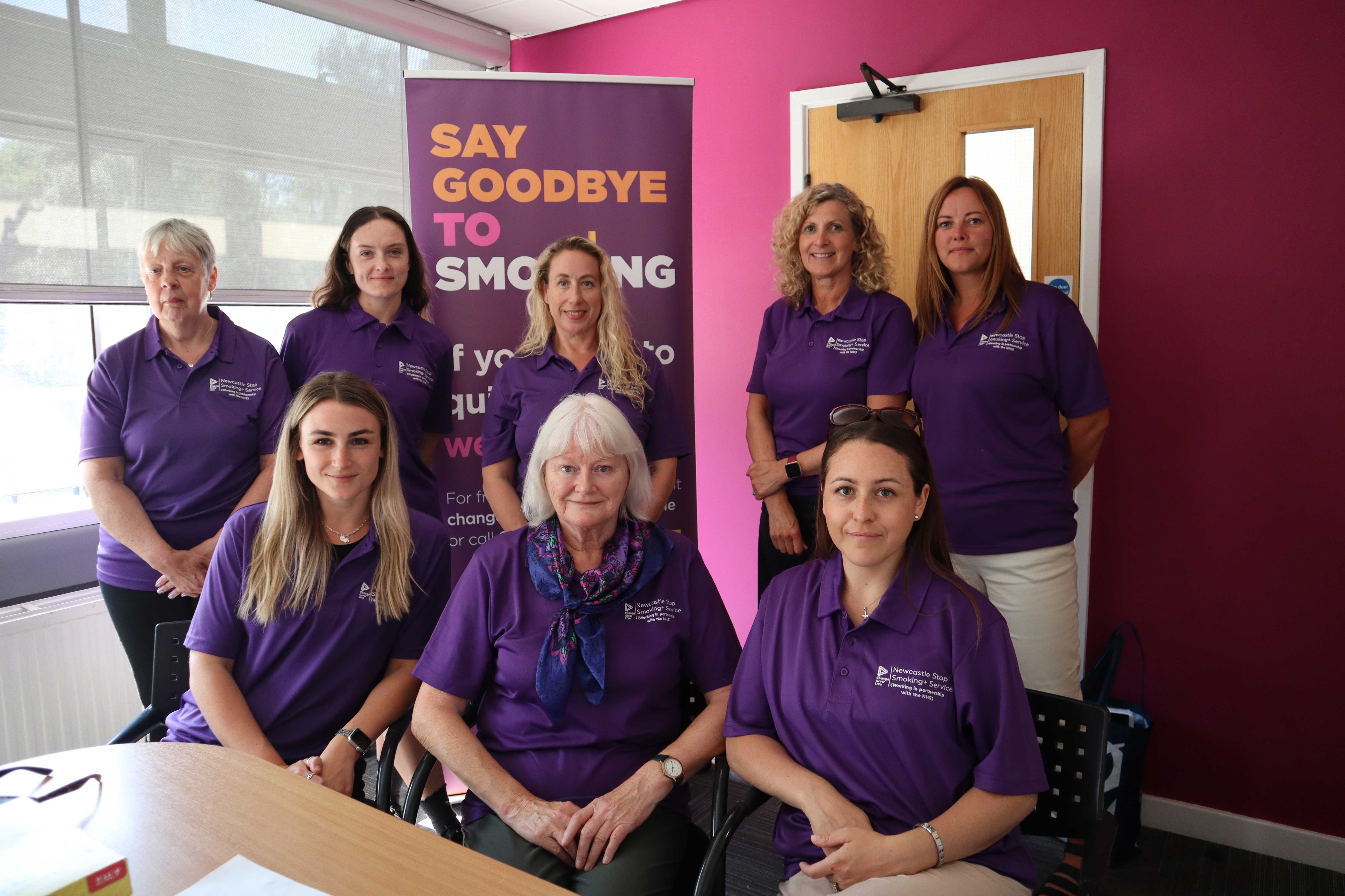 A group of women smiling at the camera all wearing purple tops