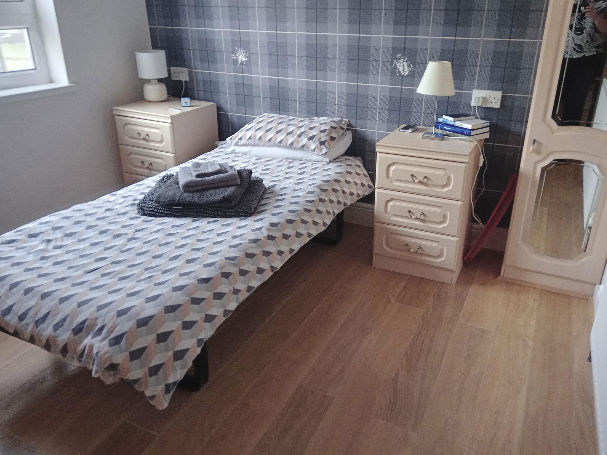 A single bed in a room with a bedside table either side and a wardrobe.