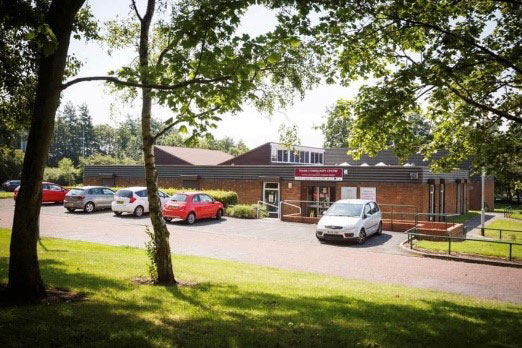 The outside of a building with a carpark in front of it surrounded by trees