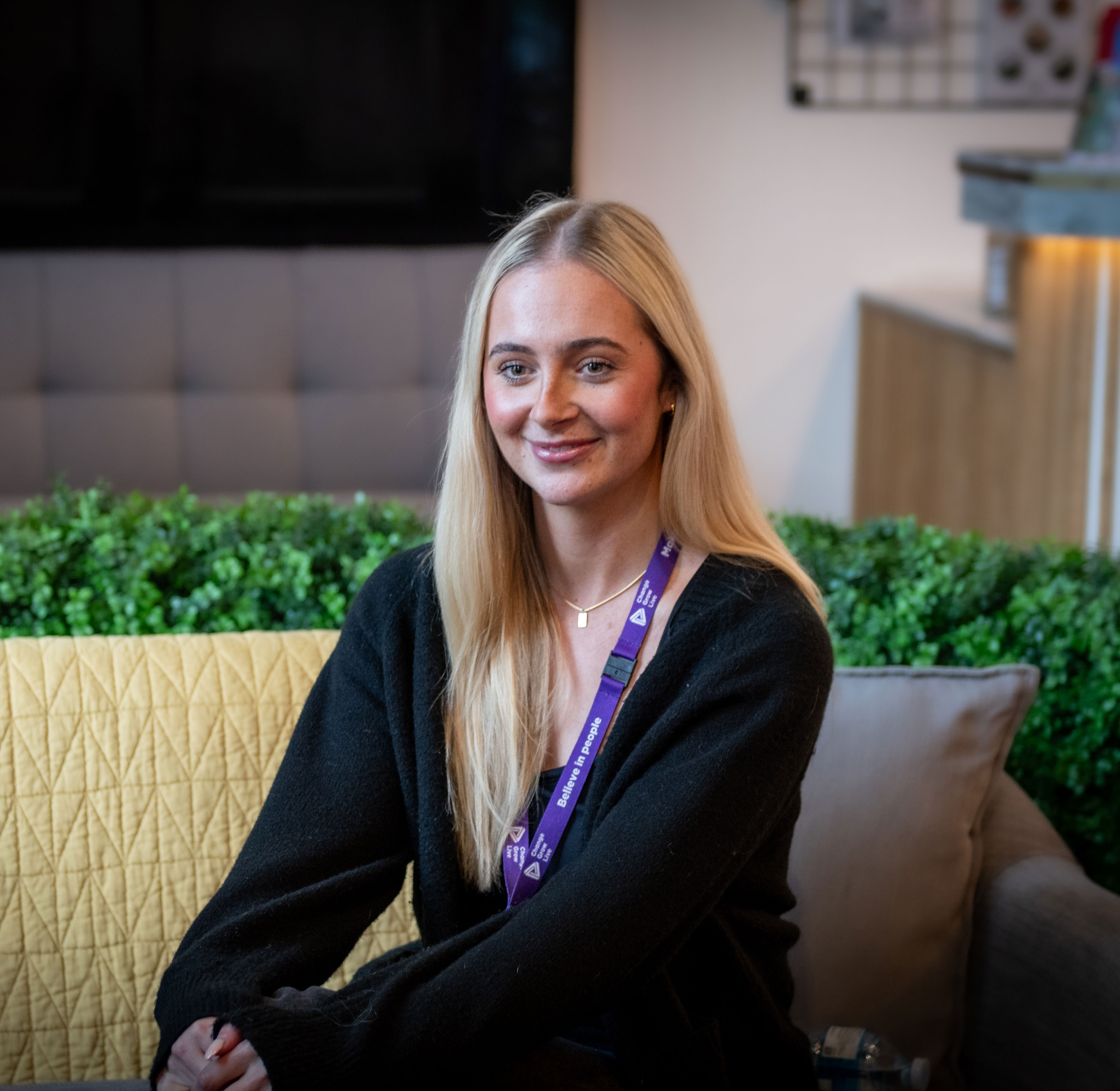 A young blonde woman sitting on a sofa looking at someone off camera