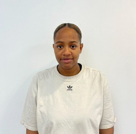 A young person stood in front of a white wall smiling at the camera