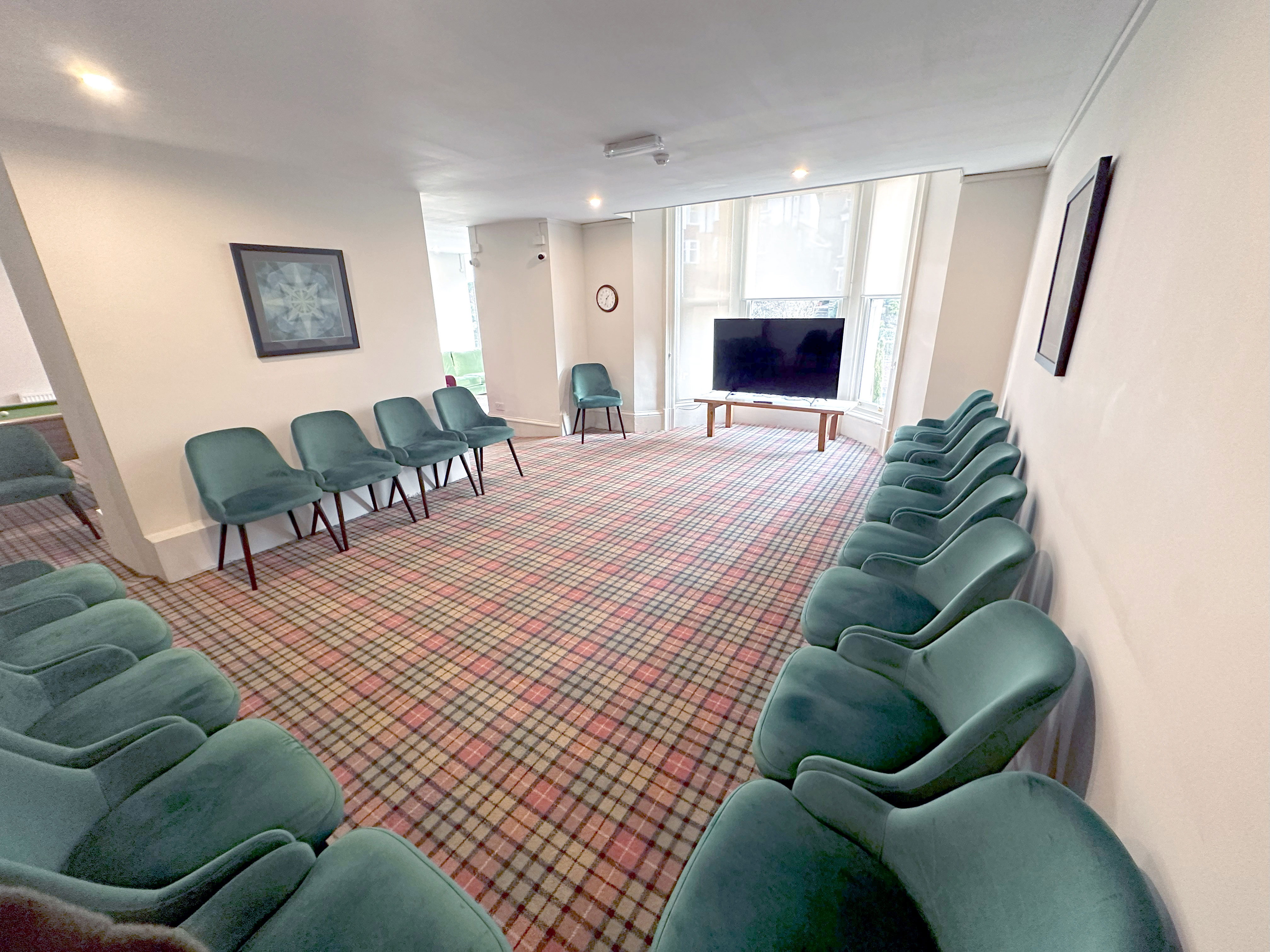 A large room with teal chairs placed around the edge and a TV at the far end