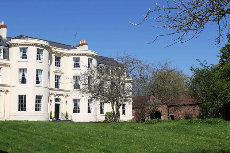 A grand manor house with a large garden in front of it