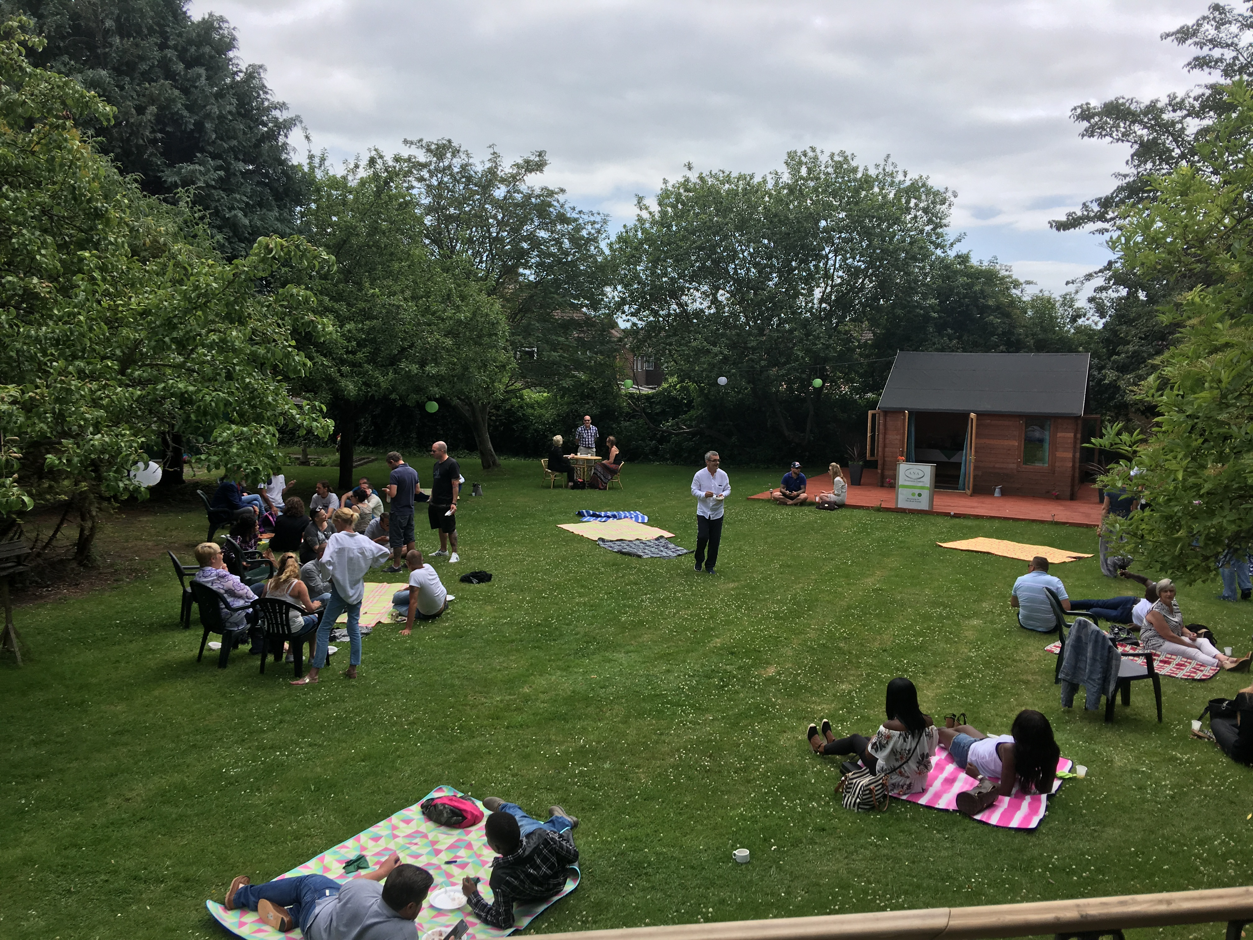 A photo of a garden. There is a big open green space with people sat around chatting.
