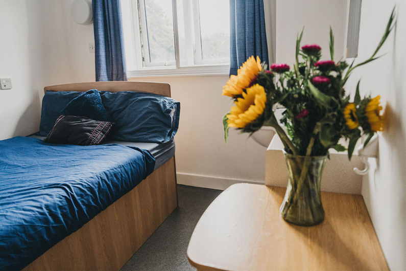 A bedroom with a vase of flowers on the sidetable