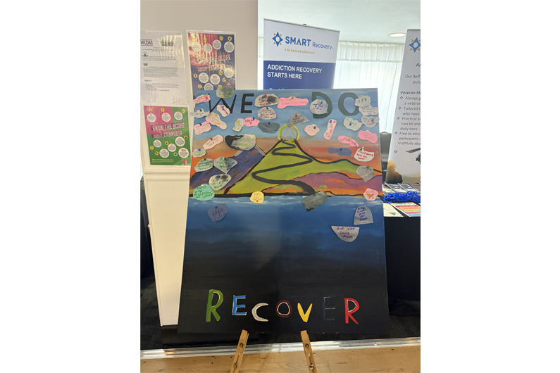 A painting of the countryside with the words We Do Recover on it and sticky notes with people sharing their thoughts on Recovery