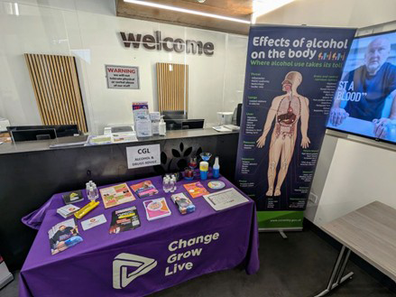 A table covered with a purple cloth and leaflets on top. A roller banner of the human anatomy is stood next to it