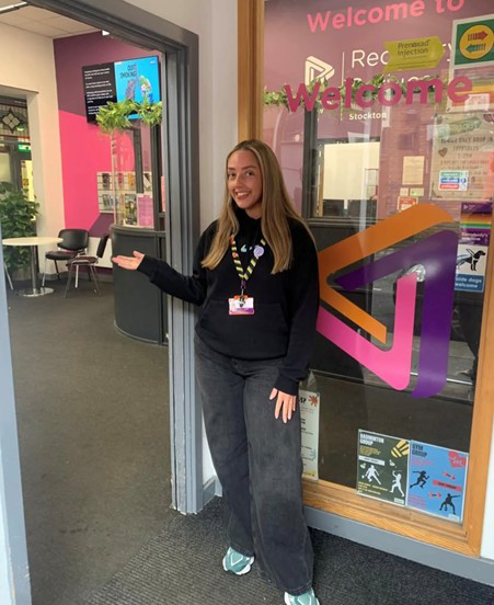 A young blonde woman stood in a reception area, gesturing to the door