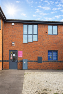 A red brick building with a pink Change Grow Live sign next to the door