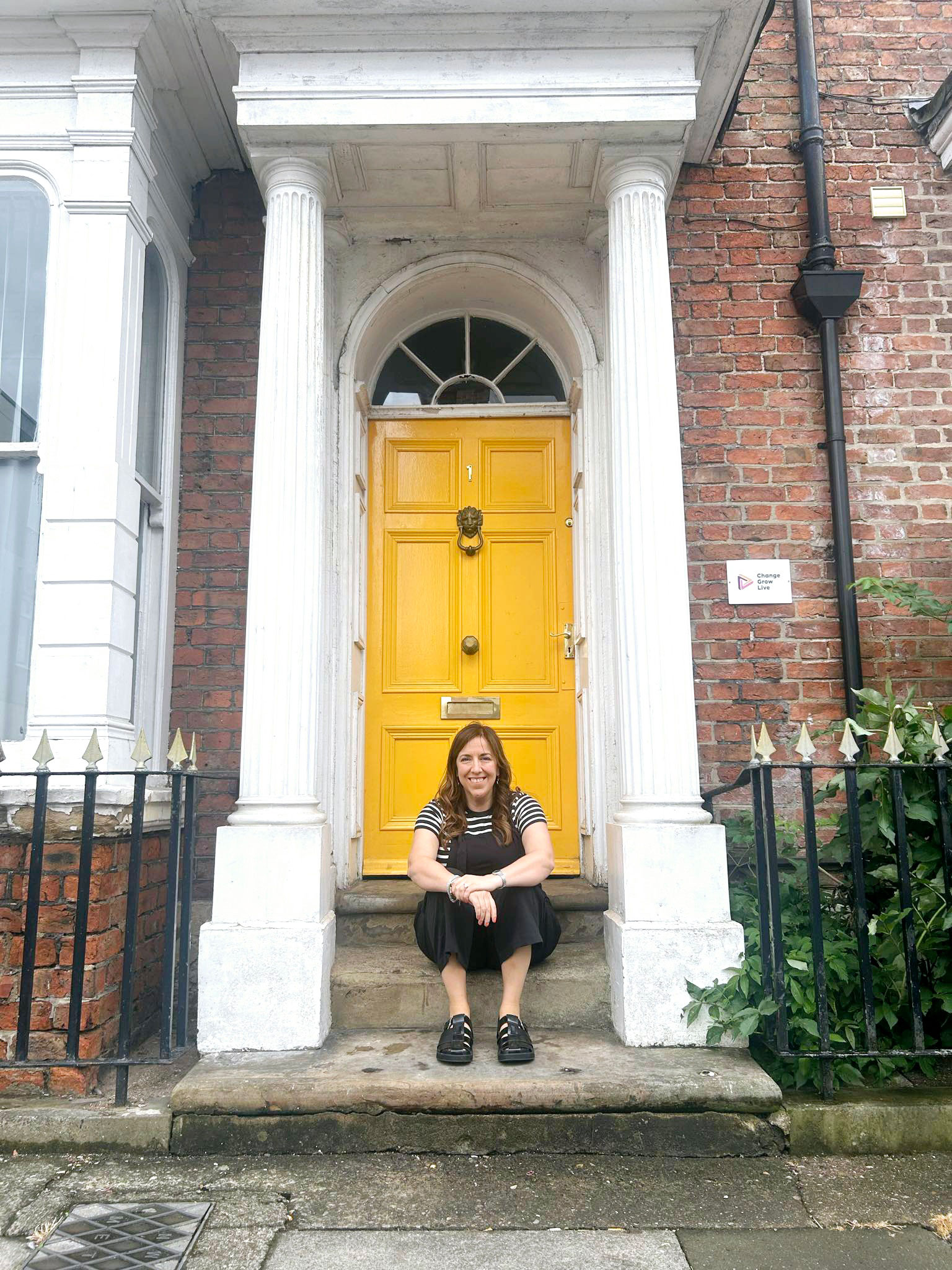 Lisa is sat on the steps outside of an old Victorian house