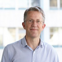 A head and shoulders photo of Martin. He is wearing a light blue shirt, and stood in front of a window.