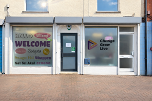 A white building with big windows either side of the front door. On the right window is the Change Grow Live logo. On the left window is the word 'Welcome' written in different languages