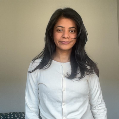 Sneha has long black hair and is wearing a white cardigan