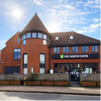 A brick building with lots of windows and a circular tower. A sign on the front reads 'Fred Winter Centre'