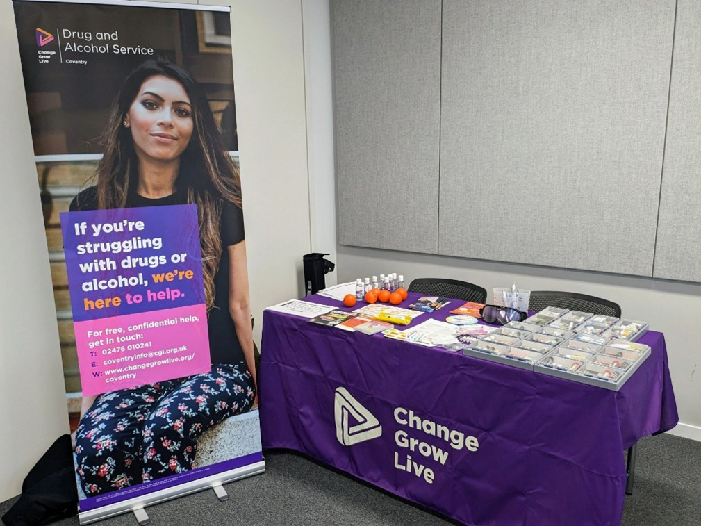 A table covered with a purple cloth and leaflets on top. A roller banner with a woman on it stands next to the table