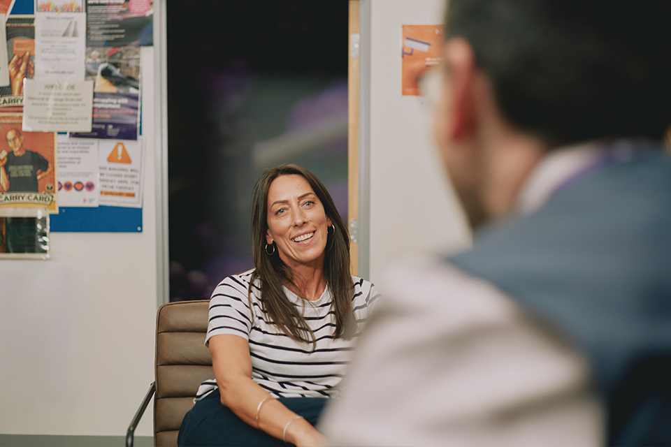 a woman in a blue and white striped t-shirt sits in a Change Grow Live service talking with a colleague