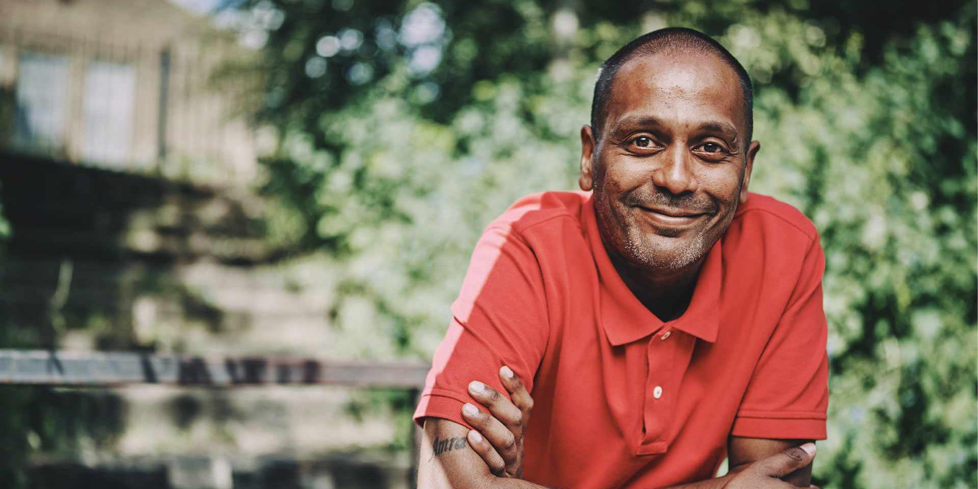 A smiling man standing in front of green leaves