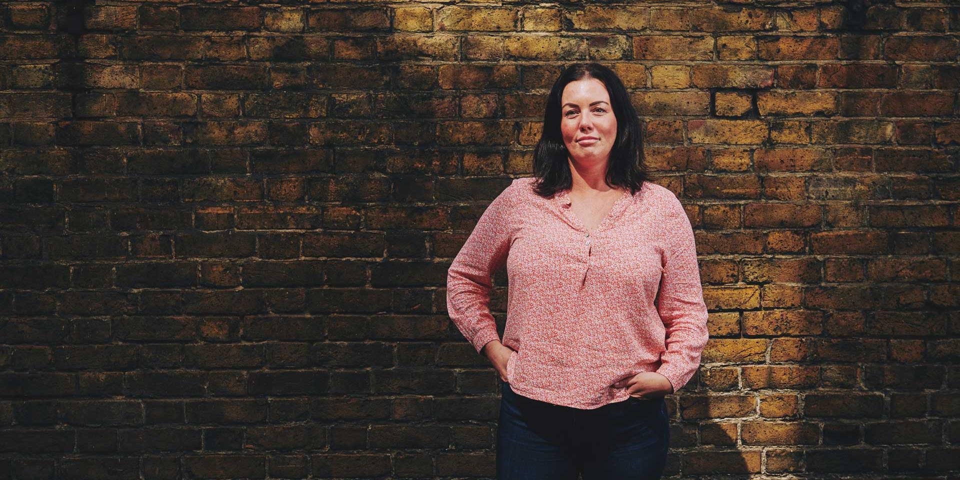 woman standing in front of a wall with her hands in her pockets