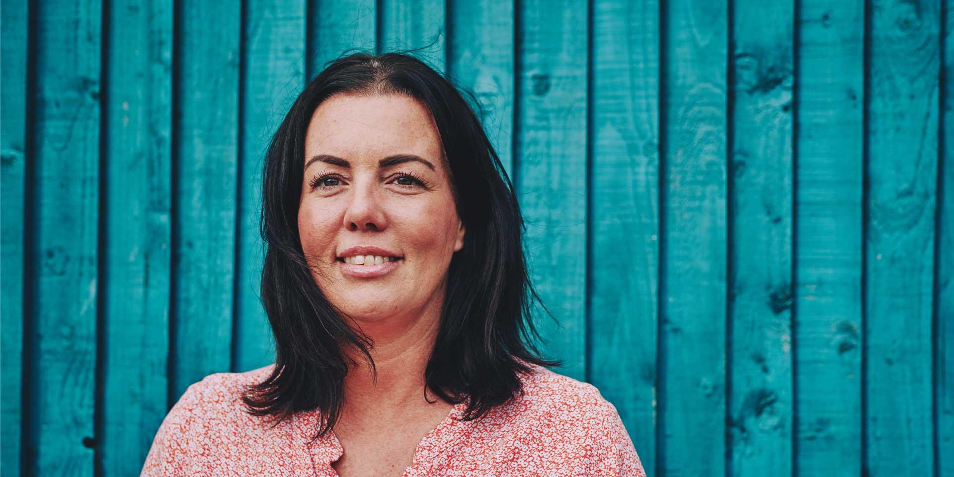 woman smiling standing against a blue wooden wall