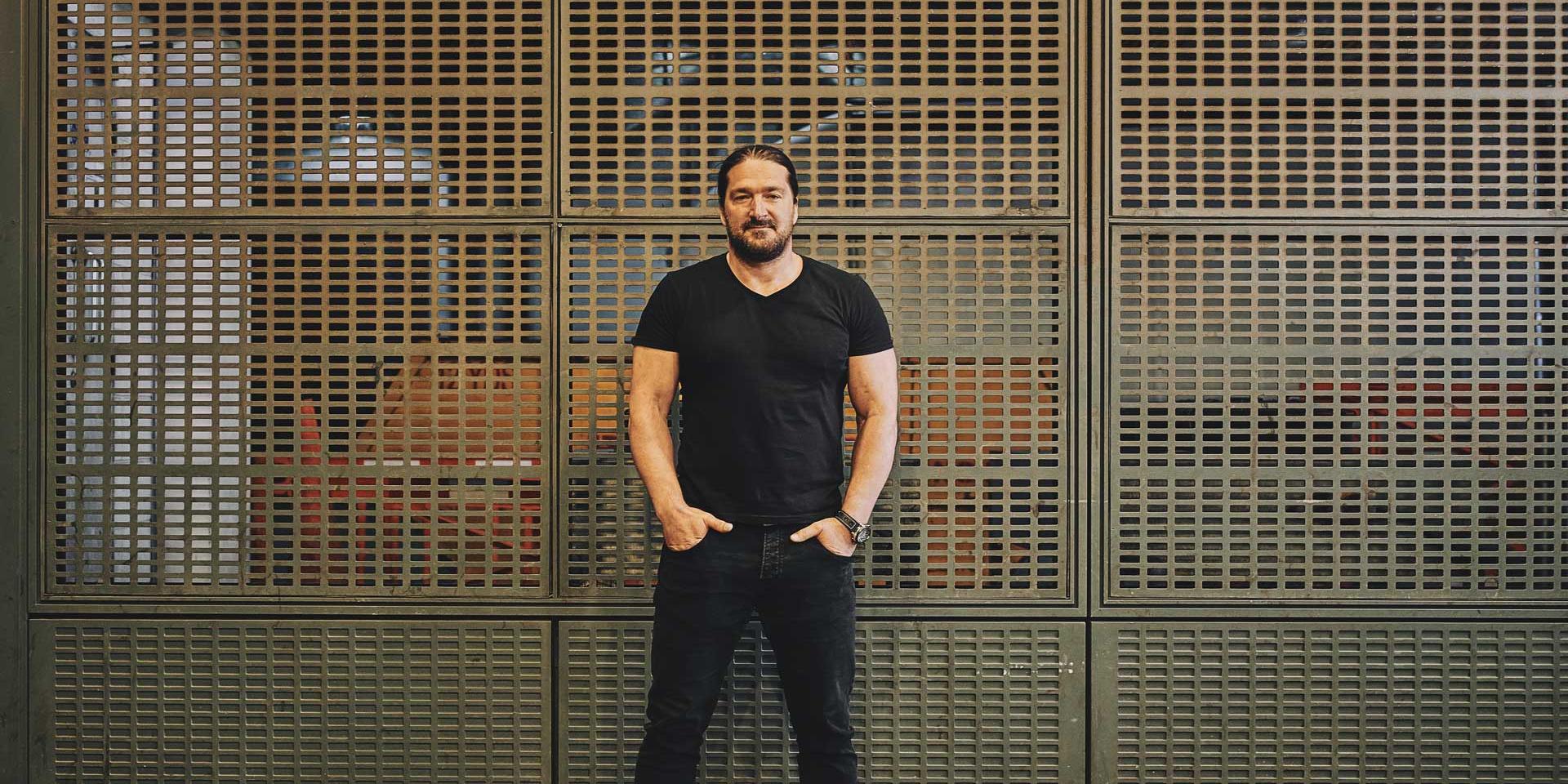 man standing with his hands in his pockets up against a metal grate