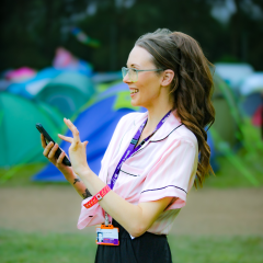 A young woman stood in front of some tents looking off to the side taking photos 