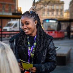 A young black woman outside smiling at someone off camera