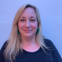 Mel has shoulder length blonde hair and is stood in front of a blue wall