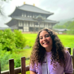 A young woman with long curly hair wearing a purple jumper
