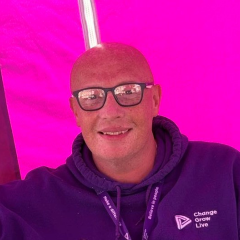 A bald man wearing glasses and a purple hoody sat inside a pink tent