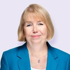 Sue has a blonde bob and is waring a white top and blue blazer