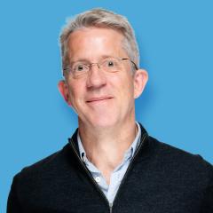 Martin has short blonde hair and is wearing glasses, light coloured shirt and black jumper