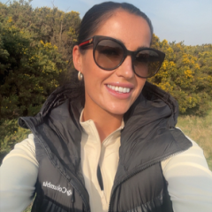 Libby is outside wearing sunglasses, a white jacket and a black bodywarmer
