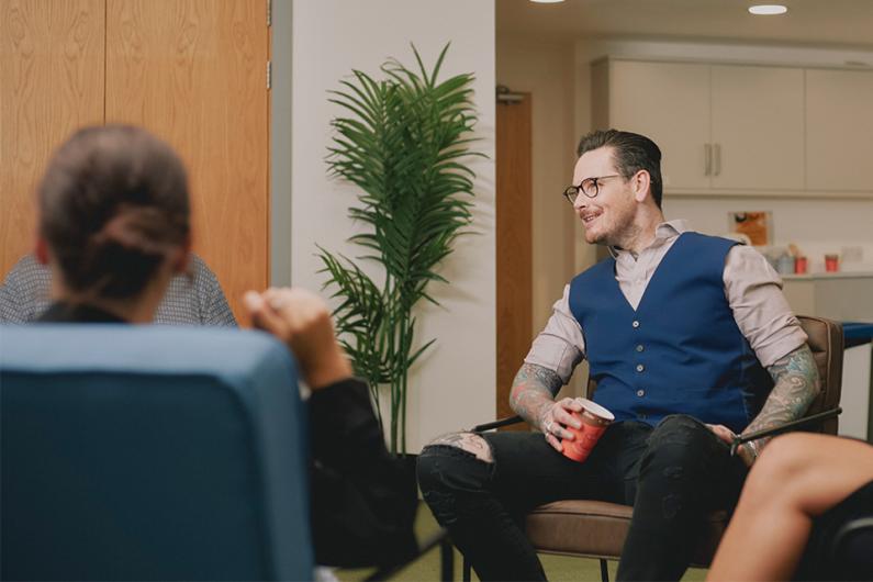 Neil sits in service relaxed drinking a coffee and chatting with colleagues