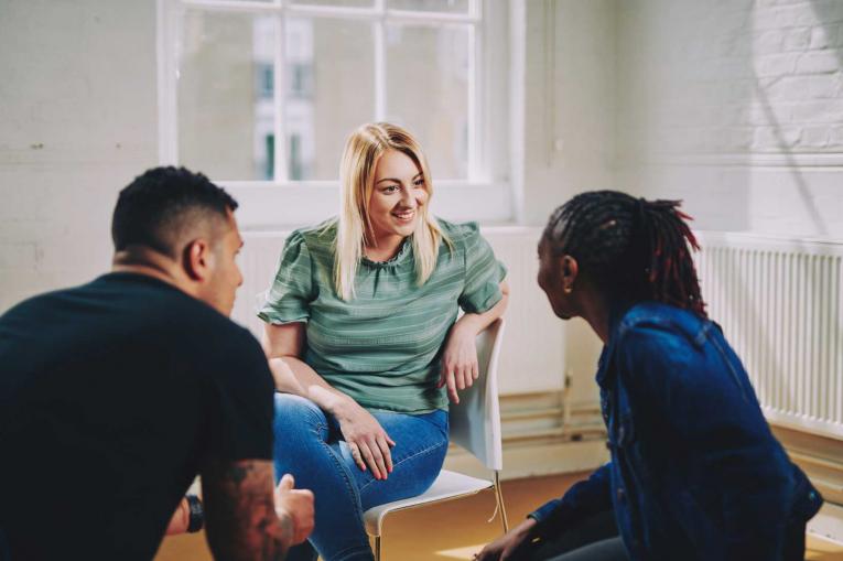 woman smiling sitting on a chair talking to two people