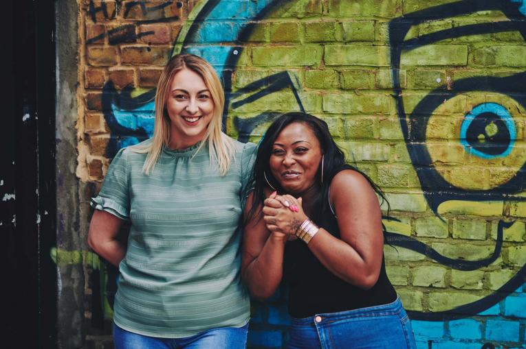 two women laughing together standing in front of some street art