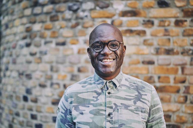 man smiling standing in front of a brick wall