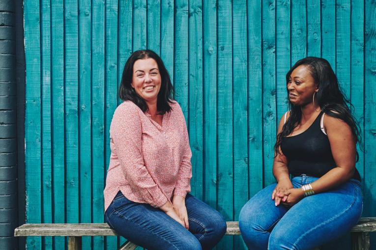 two women sitting on a bench talking and smiling