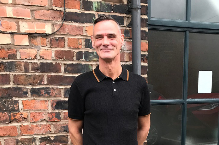 man in a black tshirt standing in front of a wall smiling