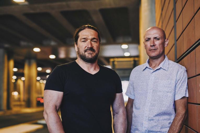 Two men are standing on the pavement