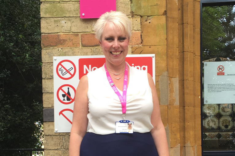 woman smiling wearing a lanyard standing in front of the service building