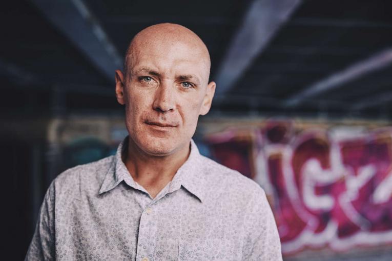 man standing in front of some graffiti under a bridge